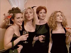 four women in black dresses are holding wine glasses and posing for the camera with their mouths open