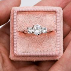 a three stone diamond ring in a pink velvet box, with two hands holding it