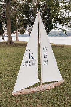 a white sailboat sitting on top of a lush green field next to trees and water