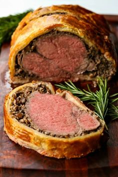 a meatloaf roll cut in half on a wooden cutting board with sprigs of rosemary