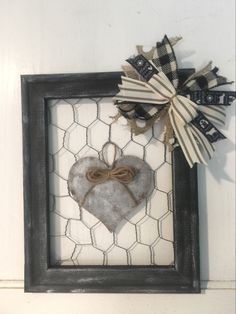 a frame with a heart hanging on the wall next to a chicken wire net and burlap bow