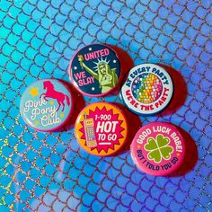 four pinback buttons with different designs on them sitting on a blue netted surface