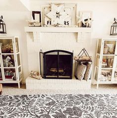 An exquisite beige-tiled fireplace, decked out with star figurines and framed artworks, rests in the center of this living room. Flanking its sides are wooden-framed cabinets displaying rustic decor, while an intricately flower-patterned gray rug anchors the space...   Image: our.simplehectic.home