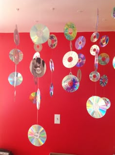 many cds are hanging from the ceiling in front of a red wall with white trim