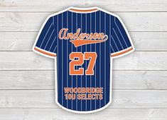 an orange and blue baseball jersey with the number 27 on it is hanging from a wooden wall