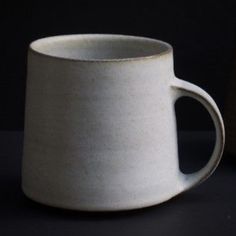 a white cup sitting on top of a table next to a black wall and a brown vase