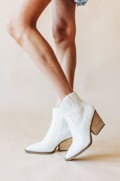 a woman wearing white cowboy boots standing on top of a wooden block heeled shoe