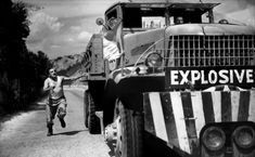 a black and white photo of a man running in front of a large truck on the road