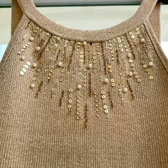 a brown sweater with gold sequins and beads on the front, hanging from a hanger