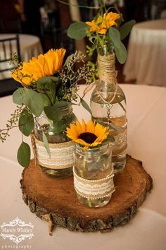 sunflowers and mason jars are sitting on a wood slice at the head table