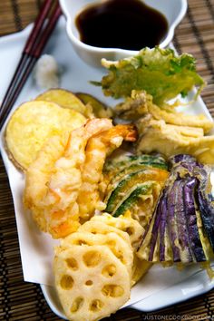 a white plate topped with different types of food next to chopsticks and sauce