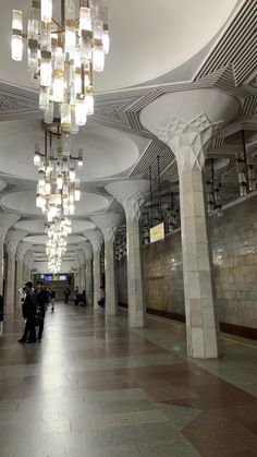 people are walking down the long hallway with chandeliers