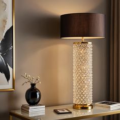 a table with a lamp on it next to a book shelf and a framed painting