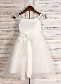 a white flower girl dress hanging on a wooden wall