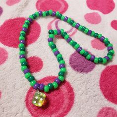 a green and purple beaded necklace with a dice charm on it's end