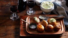 a wooden tray topped with pastries next to two glasses of wine and a bowl of mashed potatoes