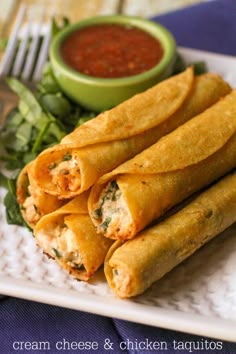 some taquitass are on a white plate next to a bowl of sauce