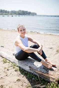 a woman is sitting on a log at the beach