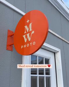 an orange sign hanging from the side of a gray building that says, photo shed reveal tomorrow