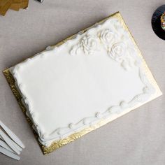 a white cake with gold trim sitting on top of a table next to two forks