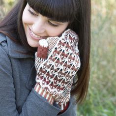 a young woman smiles as she holds her mittens up to her face