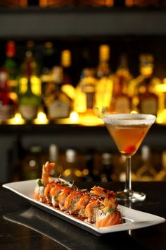 a white plate topped with sushi next to a cocktail glass on a bar counter