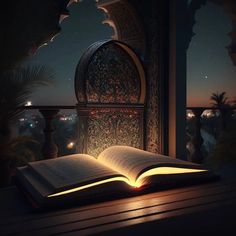 an open book sitting on top of a wooden table next to a window at night