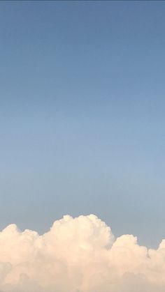 an airplane is flying high in the sky above some white fluffy clouds on a clear day