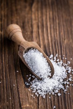 a wooden spoon filled with sea salt on top of a table