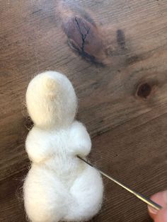 someone is needleing the wool on top of a small white teddy bear ornament