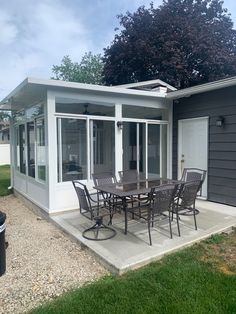 a patio with table and chairs in front of a gray house that has white trim on the walls