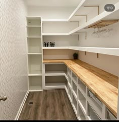 an empty walk in closet with white shelves and wooden counter tops, along with wood flooring