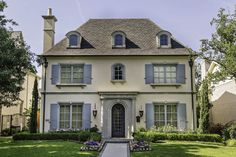 a white house with blue shutters on the front and side windows, surrounded by lush green grass