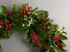 two christmas wreaths with red berries and greenery on them against a gray background