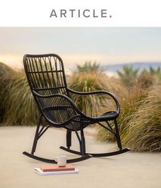 a black rocking chair sitting on top of a cement ground next to tall grass and plants