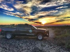 a pickup truck parked on the side of a dirt road in front of a sunset