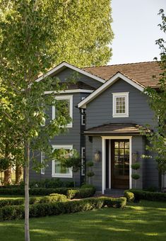 a gray house with white trim and brown shingles on the roof, surrounded by green grass