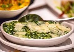 a white bowl filled with spinach and cheese next to other dishes on a table