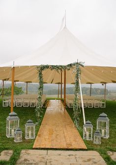 an outdoor wedding setup with lanterns and greenery on the grass under a large tent