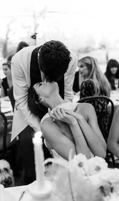 a man kissing a woman on the cheek in front of other people at a dinner table