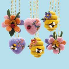 four felt heart ornaments hanging from strings with flowers and hearts attached to them on a blue background