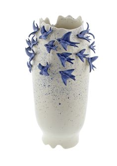 a white vase with blue flowers in it on a white background, the bottom half is covered by speckles