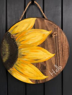 a sunflower painted on a wooden plaque hanging from a door hanger with rope