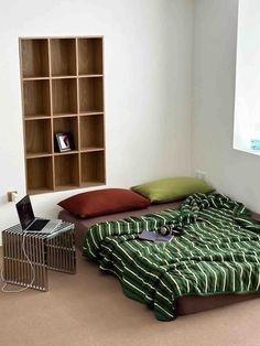 a room with a bed, bookshelf and laptop on the floor