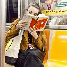 a woman sitting on a subway reading a book