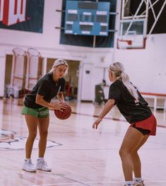 two young women playing basketball on an indoor court with the ball in her hand and one holding a basket