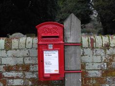 a red mailbox sitting on the side of a brick wall next to a wooden post