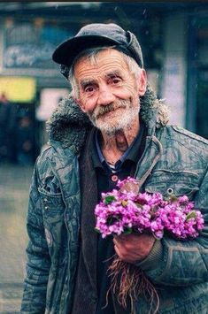 an old man is holding some flowers in his right hand and smiling at the camera