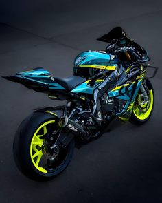 a blue and yellow motorcycle parked in a parking lot next to a black background with bright yellow rims