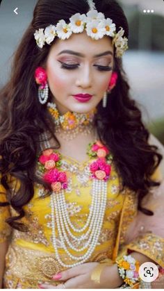 a woman with long dark hair wearing a yellow dress and flowers in her hair is looking down